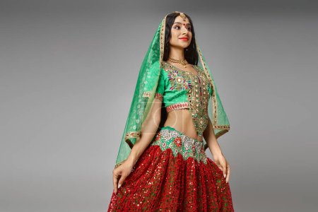 Téléchargez les photos : Attrayant jeune femme indienne en costume traditionnel avec des accessoires posant sur fond gris - en image libre de droit