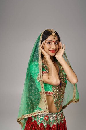 Téléchargez les photos : Jolie femme indienne en vêtements nationaux avec bindi et voile regardant caméra, mains près du visage - en image libre de droit