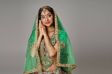Téléchargez les photos : Attrayant modèle féminin indien en costume national avec voile et bindi posant sur fond gris - en image libre de droit