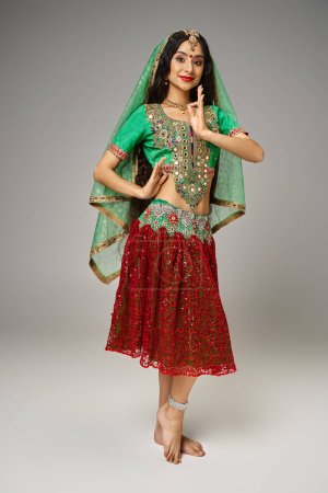 Téléchargez les photos : Joyeuse belle femme indienne en choli traditionnel et jupe gestuelle et regardant la caméra - en image libre de droit