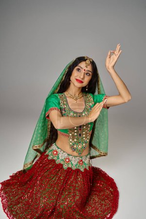 Téléchargez les photos : Attrayant modèle indien féminin avec point bindi sur le front posant sur le sol et gesticulant avec les mains - en image libre de droit