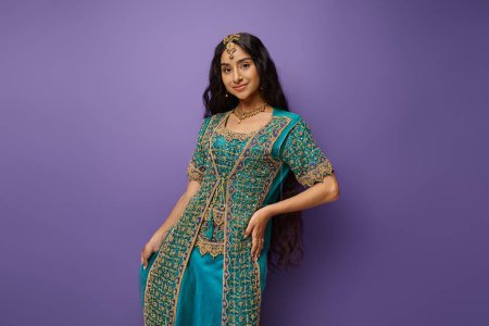 Photo for Good looking young indian woman in traditional blue sari posing with hand on hip on purple backdrop - Royalty Free Image