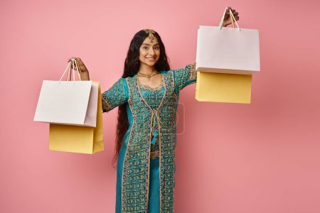 Photo for Cheerful indian woman in traditional blue sari posing with shopping bags in hands smiling at camera - Royalty Free Image