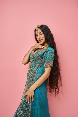 Photo for Vertical shot of jolly beautiful indian woman in blue sari with accessories posing on pink backdrop - Royalty Free Image
