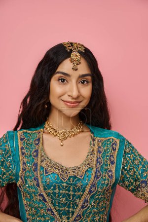 Photo for Vertical shot of young indian woman in blue sari with accessories smiling at camera on pink backdrop - Royalty Free Image