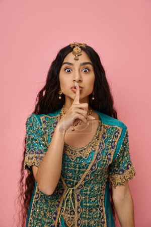 Photo for Vertical shot of young pretty indian woman in blue sari showing silence gesture looking at camera - Royalty Free Image