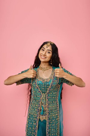 Photo for Vertical shot of young indian woman in blue sari showing thumbs up gesture and smiling at camera - Royalty Free Image