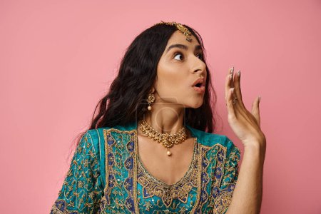 Photo for Amazed young indian woman in traditional blue sari posing with hand near mouth on pink background - Royalty Free Image