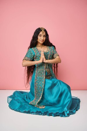 Photo for Young beautiful indian woman in traditional blue sari showing praying gesture on pink backdrop - Royalty Free Image