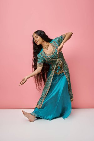 Photo for Good looking indian woman in traditional blue sari gesturing while dancing on pink background - Royalty Free Image