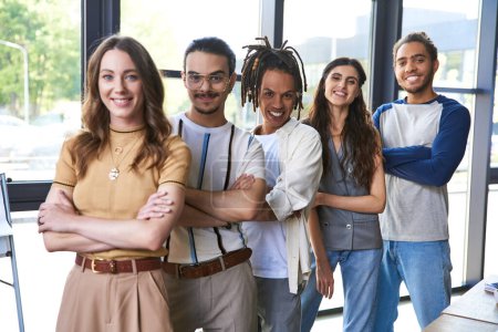group portrait of confident interracial entrepreneurs standing with folded arms in modern office