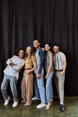 joyful multiethnic startup team posing on black backdrop in modern coworking office, group portrait