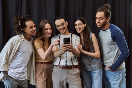 cheerful manager using smartphone near multicultural team on black backdrop in office, group photo