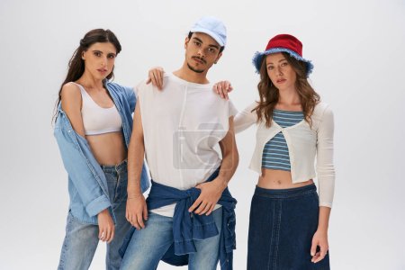 trendy man and fashionable women in street style outfits looking at camera on grey backdrop