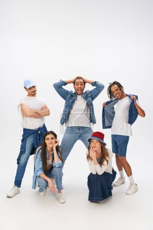 Photo for Excited multicultural men posing near stylish women squatting on grey backdrop, street style - Royalty Free Image
