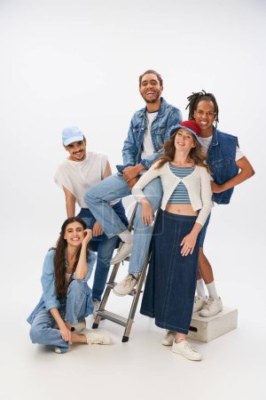 Photo for Joyful multicultural friends in trendy clothes posing with ladder and looking at camera on grey - Royalty Free Image