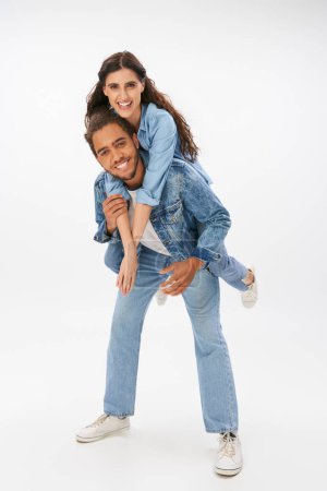 Photo for Stylish african american man piggybacking happy girlfriend in denim clothes on grey, full length - Royalty Free Image