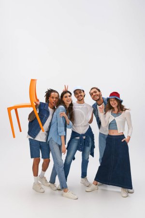 Photo for African american man posing with orange chair near stylish interracial friends having fun on grey - Royalty Free Image