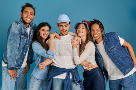 Photo for Cheerful and trendy multicultural friends posing near young man in cap on blue, modern fashion - Royalty Free Image