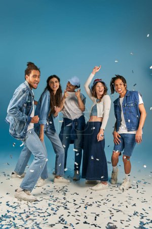 excited multiethnic friends in stylish casual clothes smiling near sparkling confetti, party time