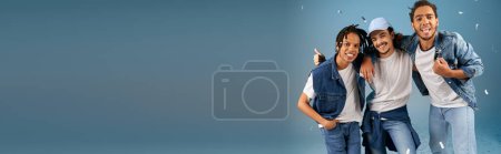 Téléchargez les photos : Amis multiethniques joyeux dans des vêtements décontractés à la mode posant sous confettis festifs sur bleu, bannière - en image libre de droit