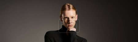 young non binary model in black turtleneck looking at camera with hand under chin, fashion, banner