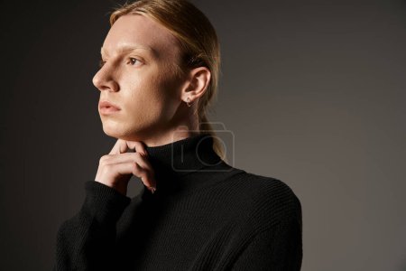 good looking young non binary person in black turtleneck with fist under chin looking away, fashion