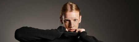 young non binary model touching collar of black turtleneck and looking at camera, fashion, banner