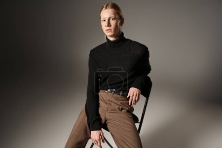 attraktives nicht binäres Modell in schwarzem Rollkragen mit Pferdeschwanz auf schwarzem Stuhl sitzend, Mode