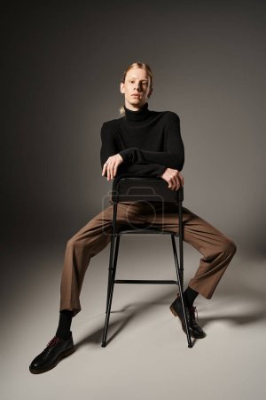 vertical shot of young non binary person with red hair and ponytail sitting on black chair