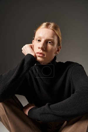 vertical shot of young non binary model sitting on floor with crossed legs and looking at camera