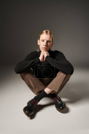 vertical shot of young non binary model in black turtleneck sitting on floor with crossed legs