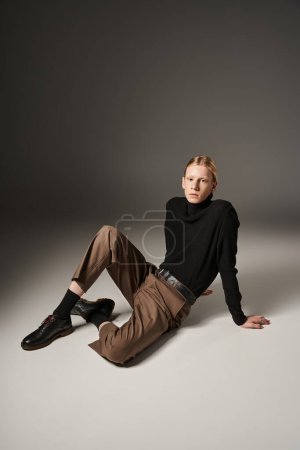 attractive young non binary model with ponytail posing on floor and looking at camera, fashion