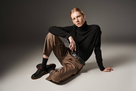 junge nicht binäre Person in schwarzem Rollkragen, die auf dem Boden sitzt und in die Kamera schaut, Modekonzept