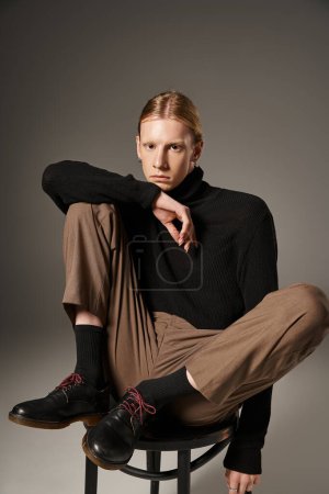 Foto de Plano vertical de joven modelo no binario en traje elegante posando en silla negra mirando a la cámara - Imagen libre de derechos