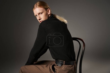 Photo for Attractive non binary person in stylish turtleneck sitting on black chair and looking at camera - Royalty Free Image