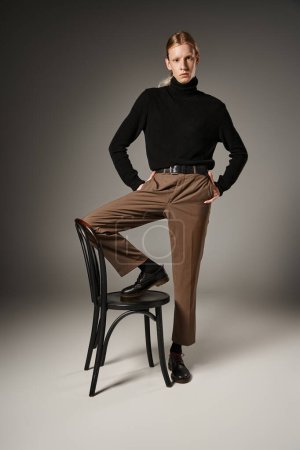 Photo for Vertical shot of non-binary person in trendy attire posing with leg on chair and hands in pockets - Royalty Free Image