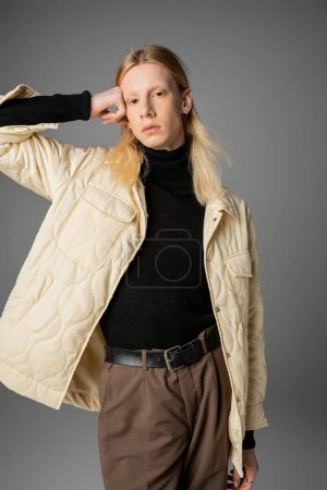 Photo for Young handsome non binary model in stylish warm outfit posing with arm raised to head, fashion - Royalty Free Image
