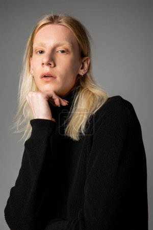 Foto de Plano vertical de joven andrógino posando en cuello alto negro de moda con puño bajo la barbilla - Imagen libre de derechos