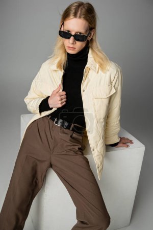 Foto de Plano vertical de joven modelo no binario en chaqueta de invierno y gafas de sol con estilo mirando a la cámara - Imagen libre de derechos