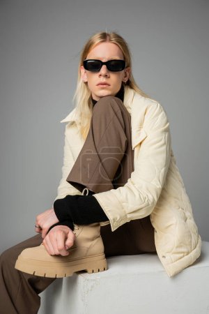 Téléchargez les photos : Belle personne androgyne en tenue d'hiver à la mode assis sur un énorme cube blanc, concept de mode - en image libre de droit