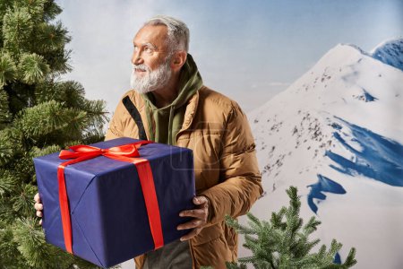 Cheerful man dressed like Santa in warm sporty jacket holding present near pine tree, winter concept