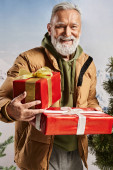 cheerful man dressed as Santa holding red presents and smiling sincerely at camera, winter concept magic mug #681087094