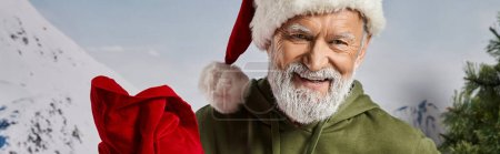 guapo Santa en sombrero de Navidad con bolsa de regalo rojo sonriendo a la cámara, concepto de invierno, pancarta