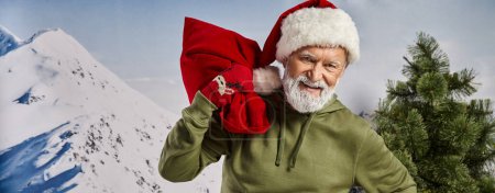 hombre atlético feliz vestido como Santa con sombrero navideño sosteniendo bolsa de regalo, concepto de invierno, bandera