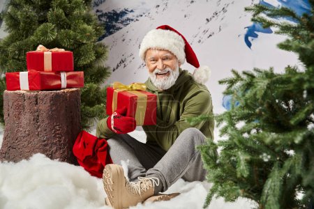 sporty Santa with white beard sitting on snow next to tree stump with presents, winter concept