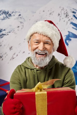 portrait of bearded Santa holding big red present wearing red hat and mittens, Christmas concept