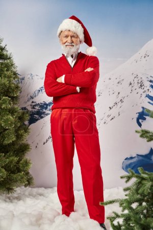 guapo Papá Noel en traje rojo y sombrero mirando a la cámara con los brazos cruzados en el pecho, concepto de invierno