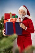 joyful man in red Santa costume holding pile of presents and smiling at camera, winter concept t-shirt #681089892