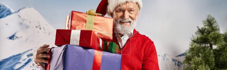 cheerful man in Santa costume with white beard showing presents at camera, winter concept, banner